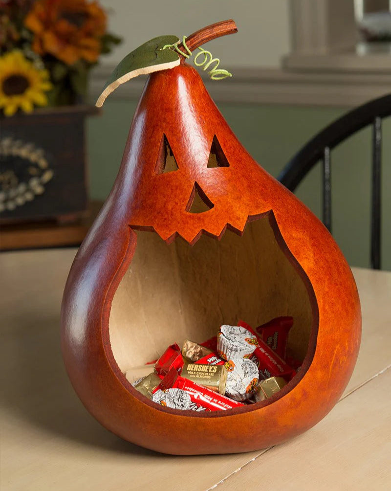 Wooden pear-shaped jack-o'-lantern with carved face, filled with candy, on a table.