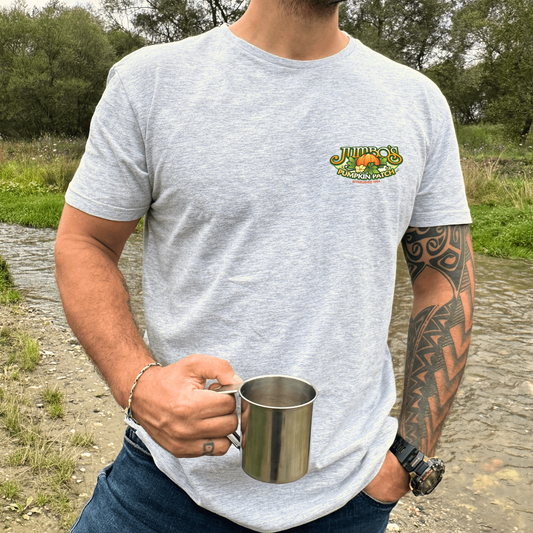 Person wearing a gray t-shirt with a logo, holding a metal cup outdoors.