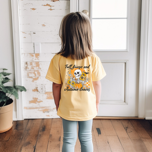 Child wearing a yellow t-shirt with autumn-themed design in a room with wooden floor and white wall.
