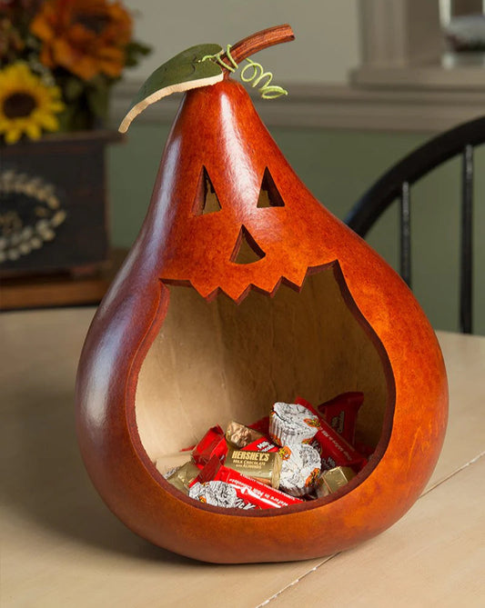 Wooden pear-shaped jack-o'-lantern with carved face, filled with candy, on a table.