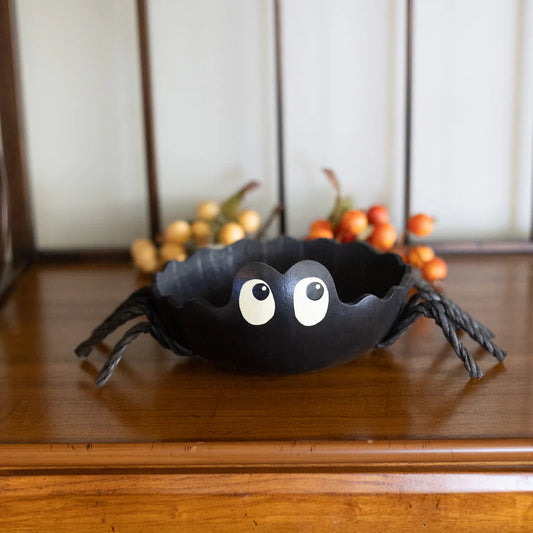 Black spider-shaped bowl on a wooden surface with decorative pumpkins in the background.